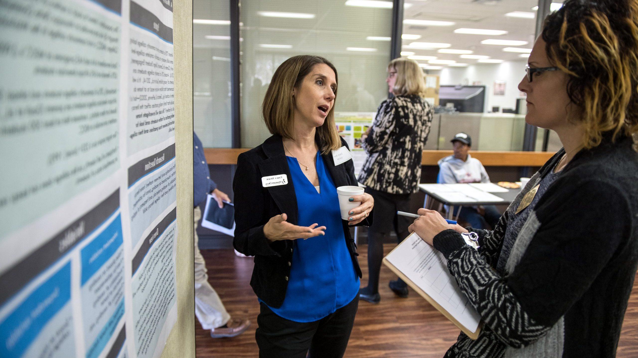 Doctoral student presenting research findings to another working professional at doctoral research student symposium.